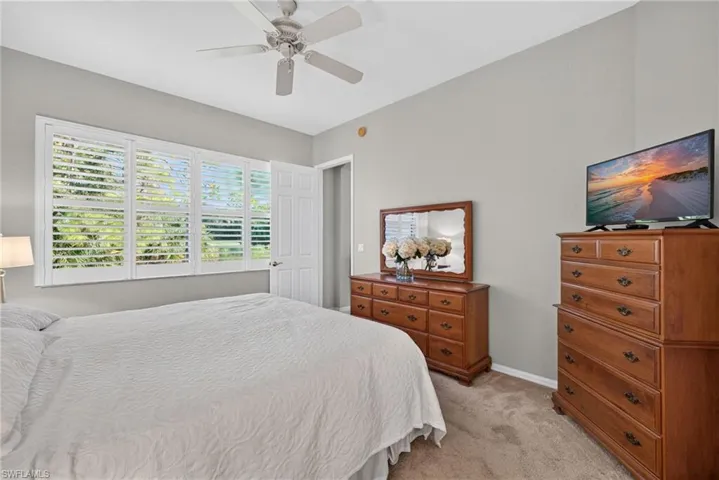 Neutral-toned room featuring plantation shutters, carpeted flooring, and a ceiling fan