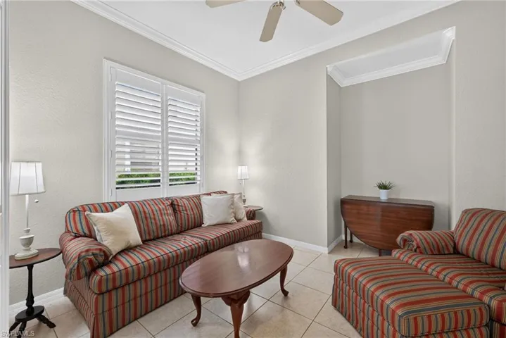 Neutral-toned interior space featuring crown molding, ceramic tile flooring, plantation shutters, and a recessed wall niche