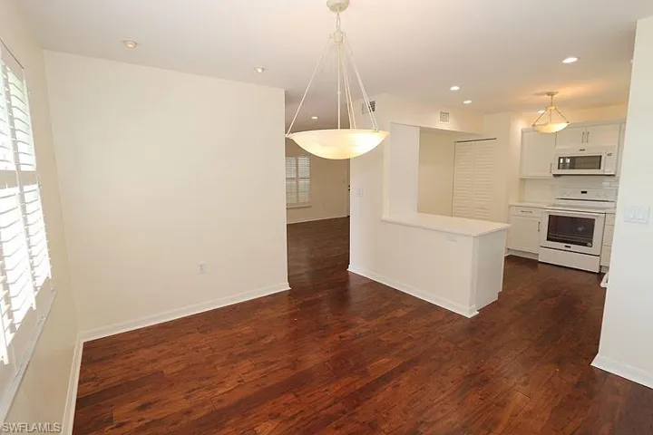 Kitchen featuring light countertops, white appliances, white cabinets, pendant lighting, and dark wood-style flooring