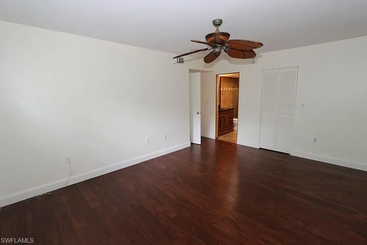 Unfurnished bedroom with dark wood-type flooring, a closet, a ceiling fan, and ensuite bathroom