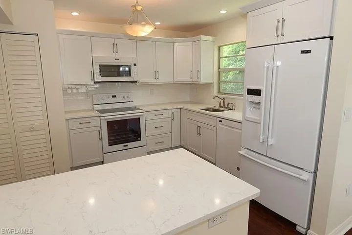 Kitchen featuring white appliances, light stone countertops, white cabinetry, and decorative backsplash