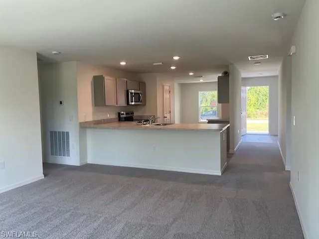Kitchen with dark colored carpet, a peninsula, appliances with stainless steel finishes, recessed lighting, and open floor plan
