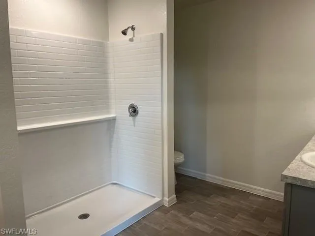 Full bathroom featuring vanity, wood finish floors, tiled shower, and a textured wall