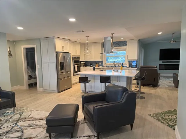 Kitchen featuring a breakfast bar, stainless steel appliances, extractor fan, hanging light fixtures, and a kitchen island with sink