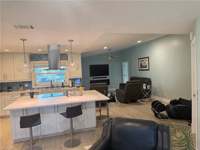 Kitchen featuring open floor plan, a kitchen bar, island range hood, white cabinetry, and lofted ceiling