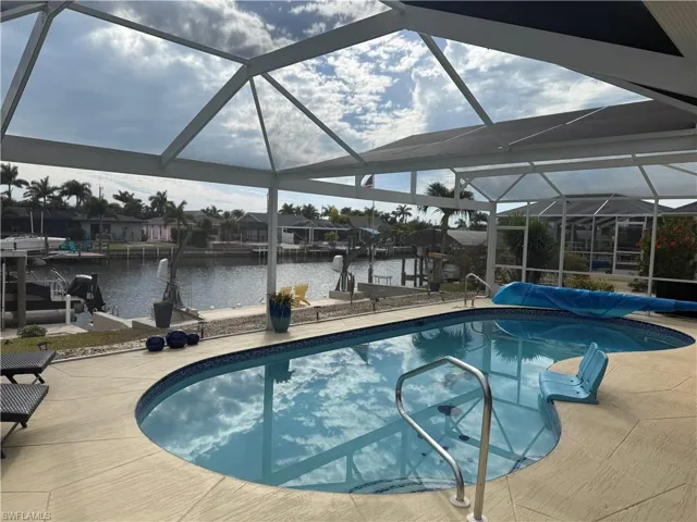 View of swimming pool featuring glass enclosure, boat lift, a boat dock, and a sunroom