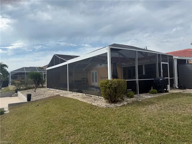 Rear view of property featuring a sunroom, glass enclosure, and a lawn