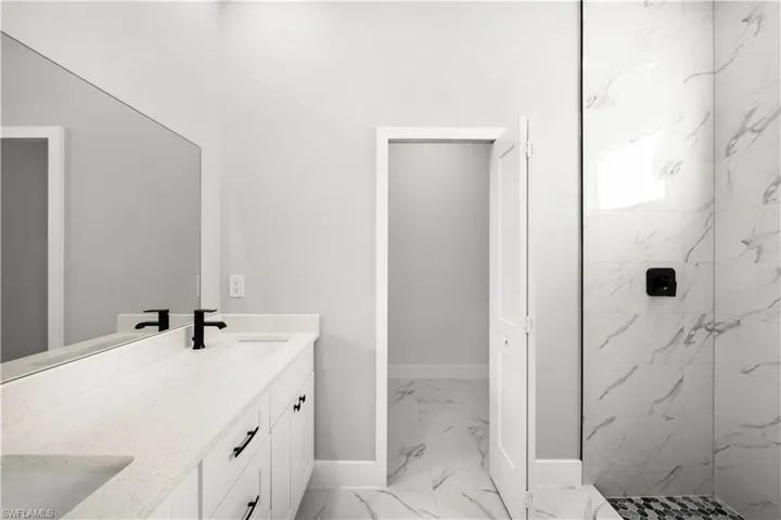 Bathroom featuring marble look tiles, double vanity, and a marble finish shower
