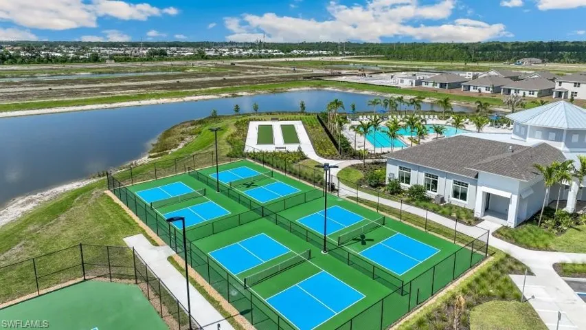 This aerial view showcases a property with multiple recreational amenities, including several outdoor courts with blue and green surfaces, and a swimming pool surrounded by palm trees