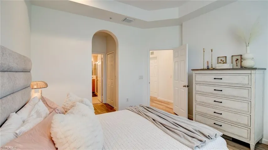 Bedroom featuring arched walkways, ensuite bathroom, light wood-style flooring, and a closet