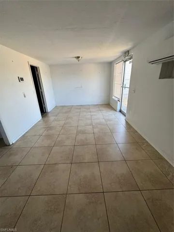 Tiled empty room with a wall unit AC and baseboards