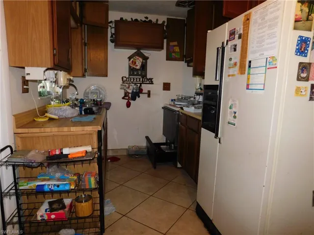 Kitchen featuring light tile patterned flooring, baseboards, and white fridge with ice dispenser