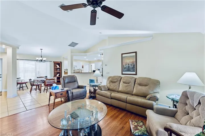 Living room featuring tile flooring, lofted ceiling, and ceiling fan with notable chandelier