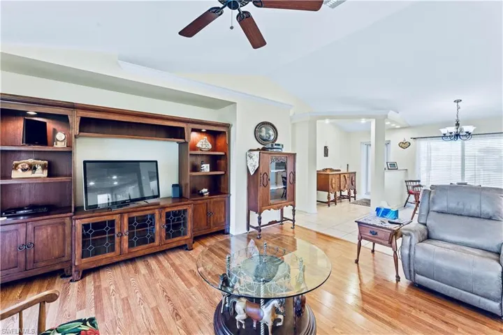 Living room featuring lofted ceiling, light wood-type flooring, and ceiling fan with notable chandelier