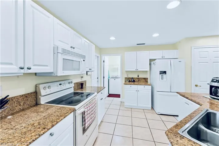Kitchen with light stone countertops, white appliances, white cabinetry, and light tile floors