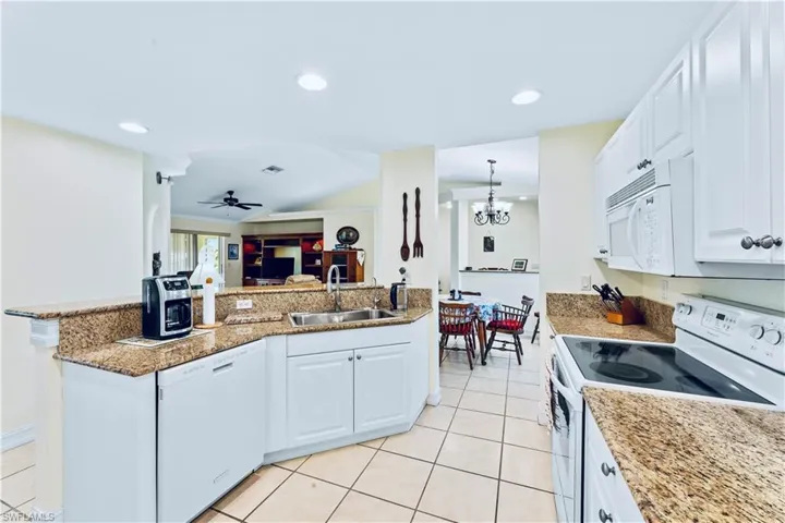 Kitchen featuring sink, white cabinets, white appliances, and light tile floors