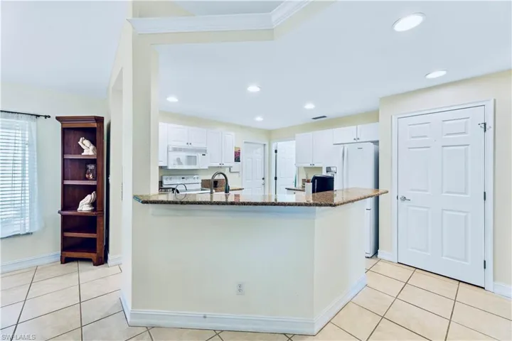 Kitchen featuring white appliances, dark stone counters, white cabinetry, and light tile floors