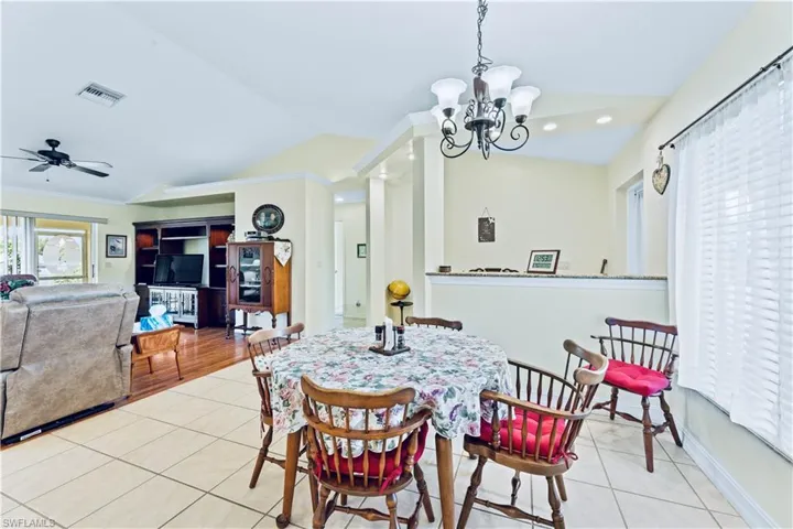 Dining area featuring ornamental molding, ceiling fan with notable chandelier, light wood-type flooring, and vaulted ceiling