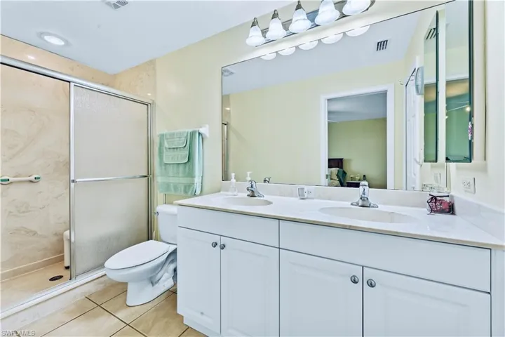 Bathroom with tile floors, a shower with shower door, double vanity, and toilet