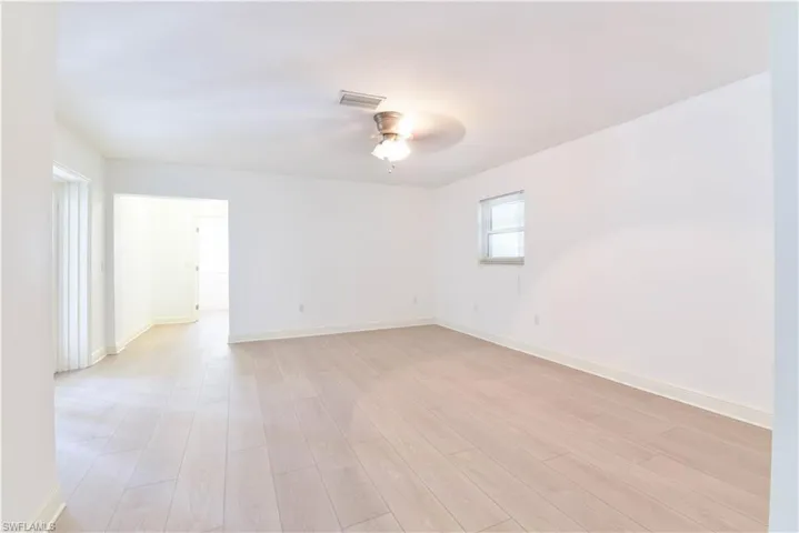 Spacious interior room featuring light wood-finish flooring, white painted walls, and a ceiling fan with integrated lighting