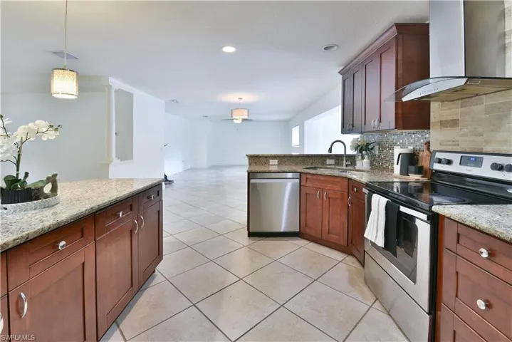 Kitchen featuring wood cabinetry, granite countertops, tile flooring, stainless steel appliances, and a mosaic tile backsplash