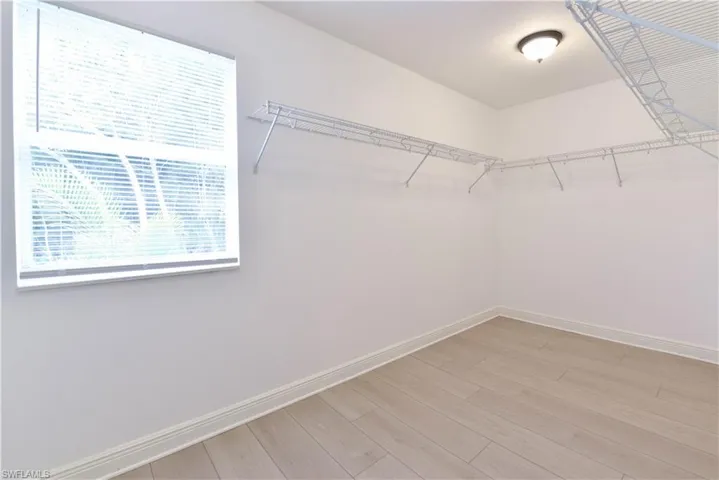 Spacious closet featuring light wood-finish flooring, white walls, and a window with blinds