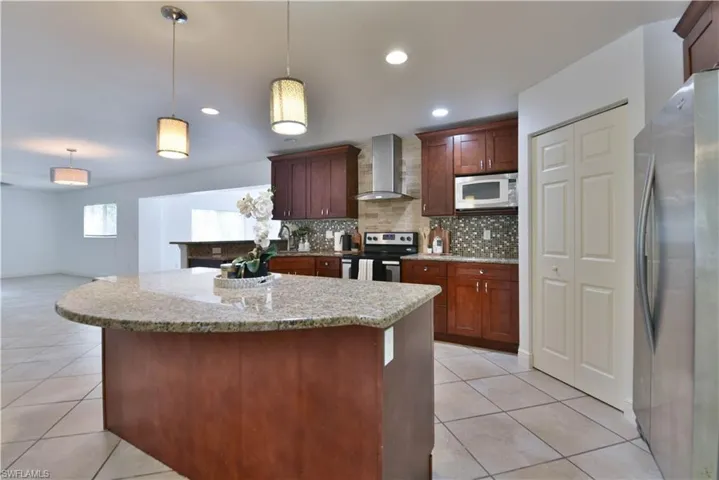 Kitchen featuring a curved central island with a granite countertop, pendant lighting, shaker-style cabinetry, and a tile backsplash