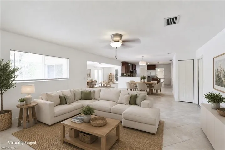 Open-concept living space featuring light tile flooring throughout, a ceiling fan with integrated lighting, and a large window with roller shades