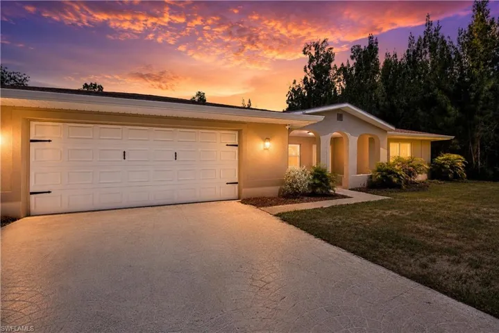 Exterior featuring a two-car garage with decorative hardware, a patterned concrete driveway, and established front landscaping
