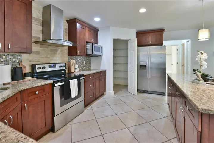 Kitchen with wood cabinetry, granite countertops, tile flooring, stainless steel appliances, and a pantry with built-in shelving