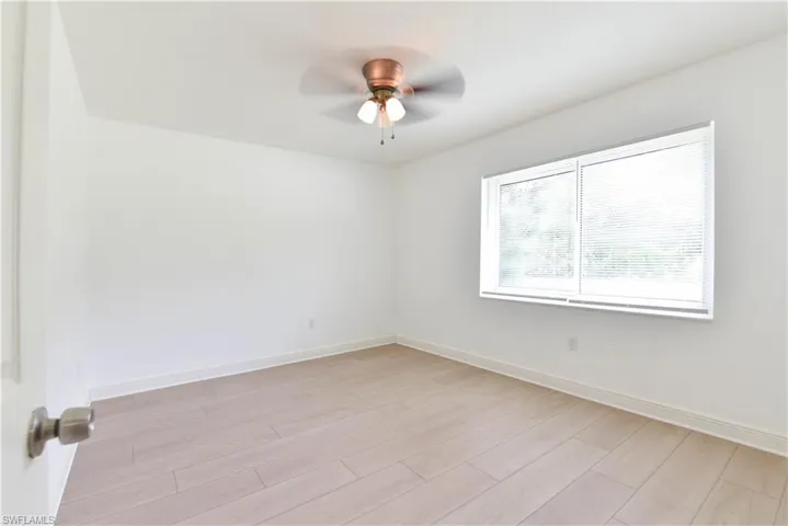 Spacious room featuring wood-finish flooring, white baseboards, and a window offering natural illumination