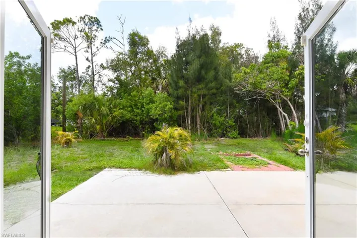 Outdoor patio with a concrete surface, providing access to a grassy area with mature trees and foliage
