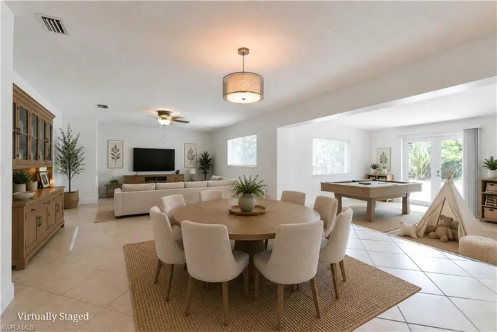 Open-concept living space featuring a dining area with a drum pendant light, tile flooring, and broad entryways