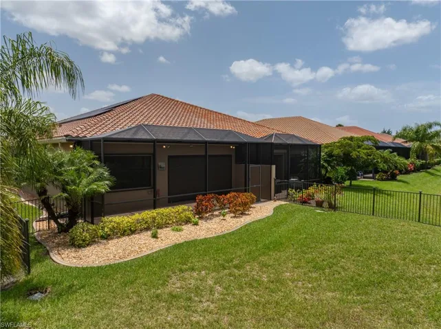 Expansive backyard featuring a manicured lawn, established landscaping, and a screen-enclosed patio with a tiled roof