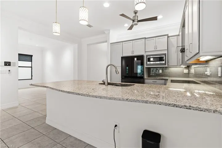Kitchen featuring a spacious island with a speckled countertop, a stainless steel sink with a high-arc faucet, light gray cabinetry, and a dark tile backsplash