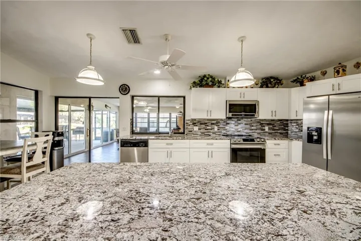 Kitchen featuring stainless steel appliances, white cabinetry, decorative light fixtures, light stone counters, and lofted ceiling