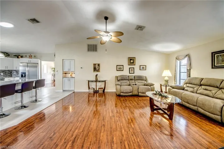 Open living room in this Cape Coral home featuring wood-finished floors, ceiling fan, and great flow for entertaining.