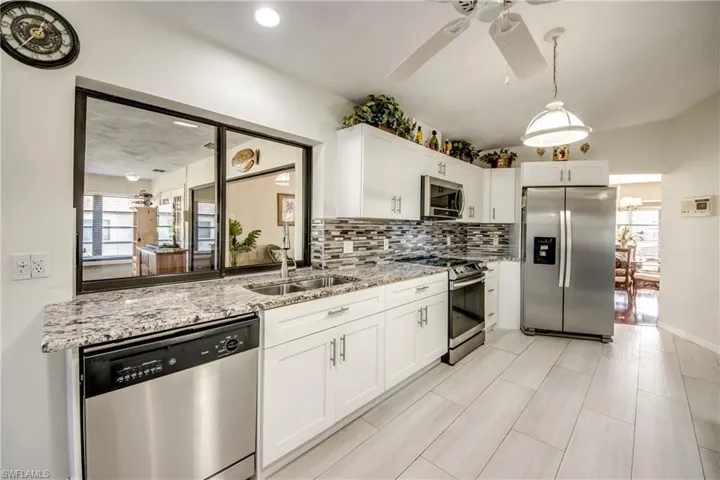Kitchen with healthy amount of natural light, stainless steel appliances, white cabinets, and light stone countertops