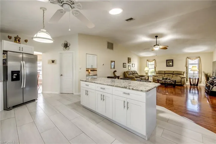 Kitchen featuring stainless steel fridge, light stone counters, a ceiling fan, white cabinetry, and lofted ceiling