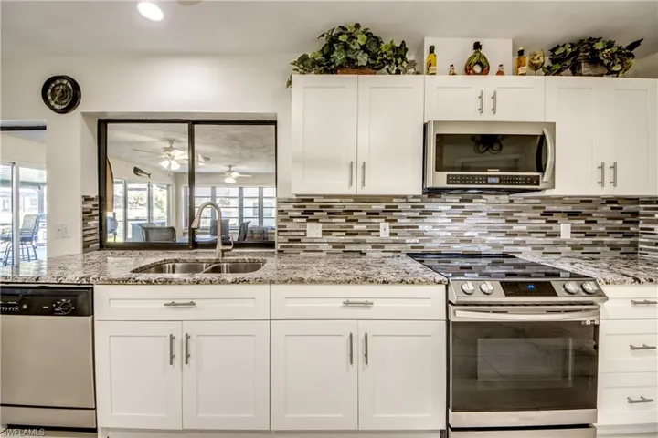 Kitchen with stainless steel appliances, white cabinetry, light stone counters, recessed lighting, and backsplash