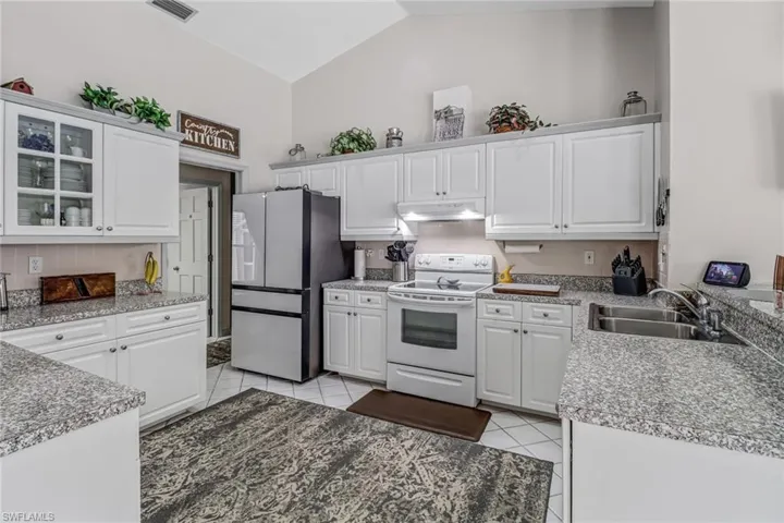 Kitchen with light tile patterned flooring, white range with electric cooktop, stainless steel refrigerator, sink, and white cabinets