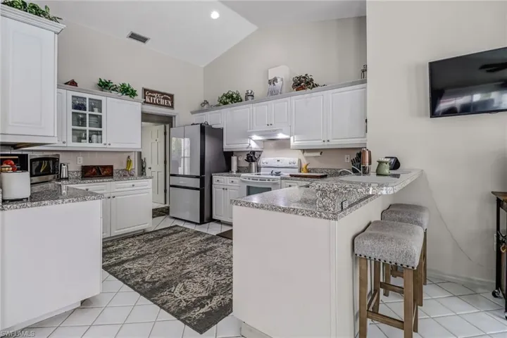 Kitchen featuring white electric range oven, white cabinetry, kitchen peninsula, light tile patterned floors, and stainless steel fridge