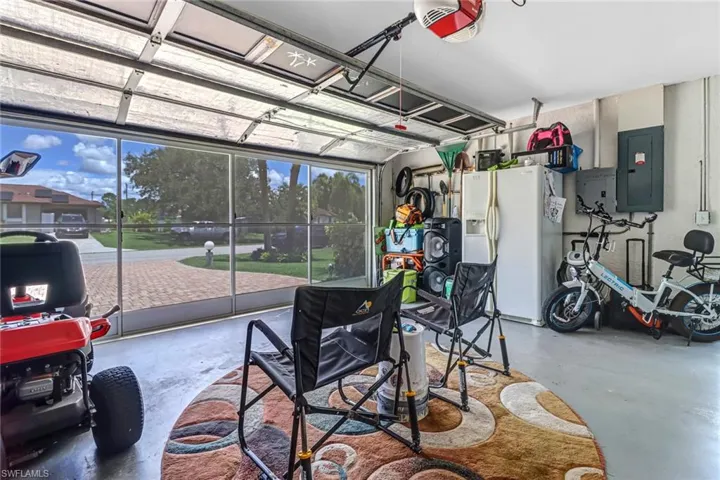 Garage with electric panel, a garage door opener, and white fridge with ice dispenser