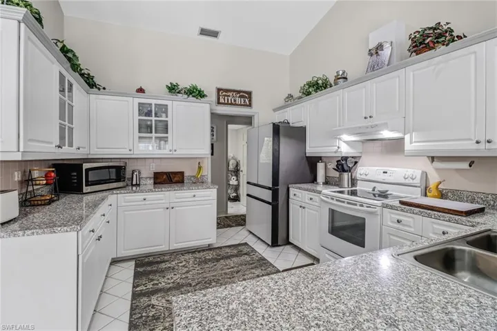 Kitchen featuring stainless steel appliances, backsplash, light tile patterned floors, vaulted ceiling, and white cabinets