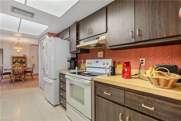 Kitchen featuring light tile patterned flooring, dark brown cabinets, white appliances, a chandelier, and decorative light fixtures