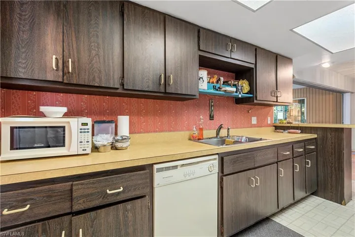 Kitchen featuring dark brown cabinets, white appliances, a skylight, sink, and light tile patterned floors