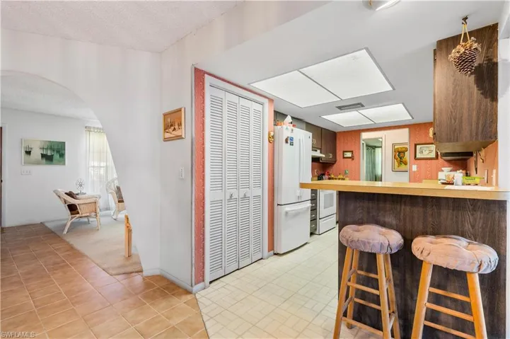 Kitchen with white fridge, light tile patterned floors, a textured ceiling, kitchen peninsula, and a kitchen bar