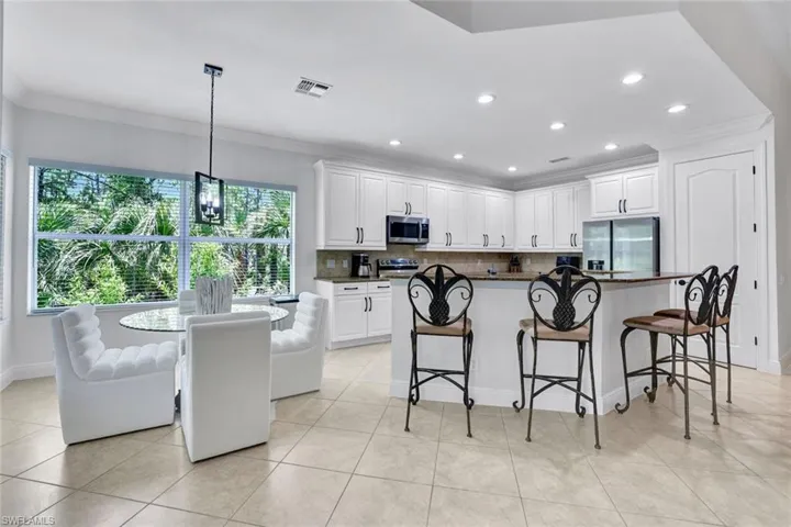 Kitchen featuring appliances with stainless steel finishes, tasteful backsplash, ornamental molding, white cabinets, and a kitchen breakfast bar