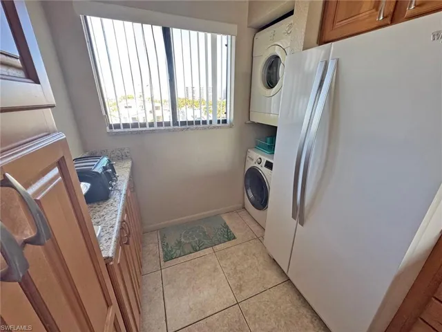 Laundry area featuring light tile patterned floors and stacked washing machine and dryer