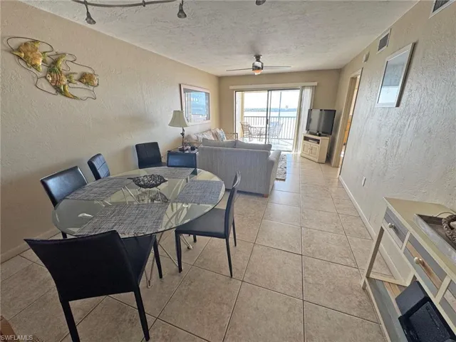 Dining/living room with a textured wall, a textured ceiling, a ceiling fan, and light tile patterned floors